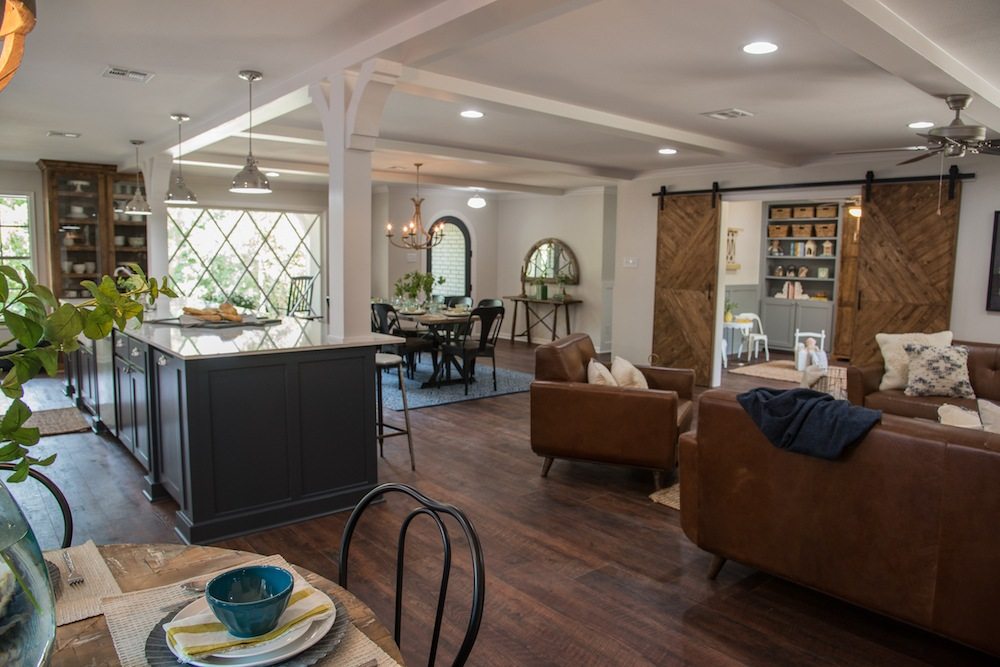 Open plan room with a dark gray kitchen island, white support columns, a dining table and sliding wood barn doors