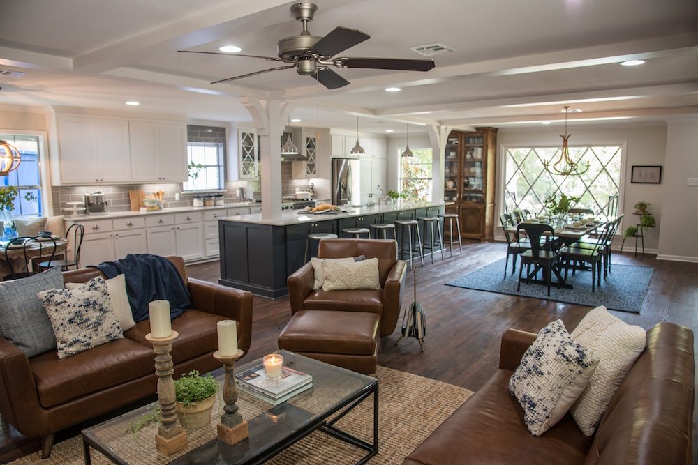 Living area with brown leather sofas and a glass coffee table, open to a dark gray kitchen island and dining area
