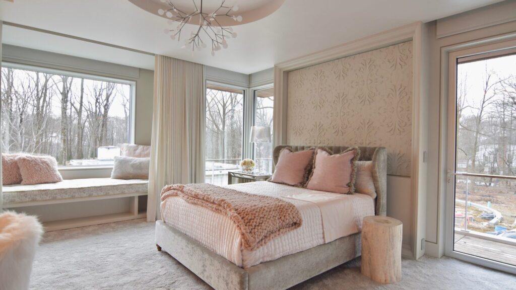 Finished bedroom with pale neutral walls, a decorative plaster panel, blush bedding and tall windows onto bare winter trees